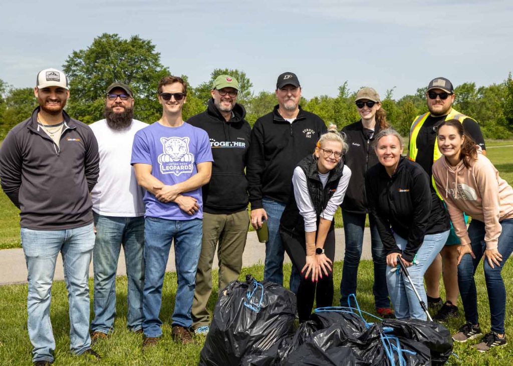 SevenGen team outdoors on a sunny day after volunteer cleanup with filled trash bags in front of them.