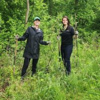 1000088973 Two volunteers smiling in wooded area.